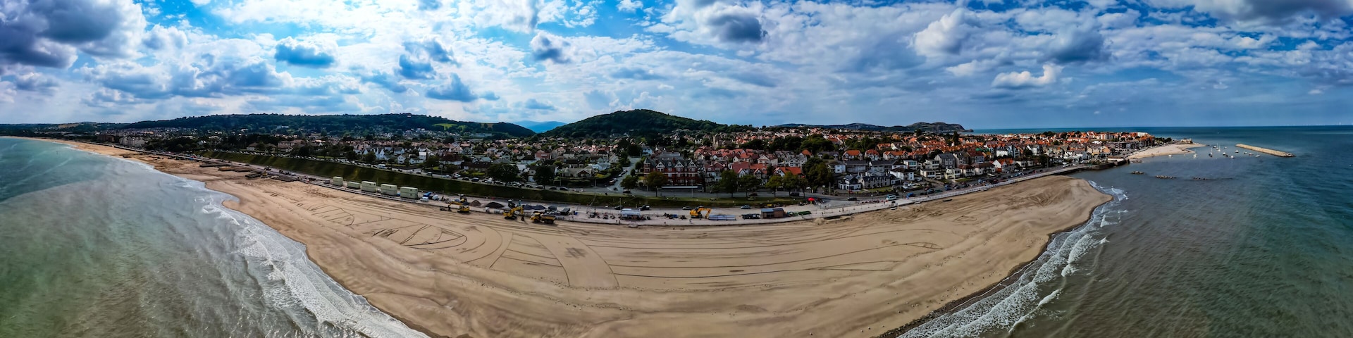 A coastal town with a beach, a harbor, and a hill in the background.