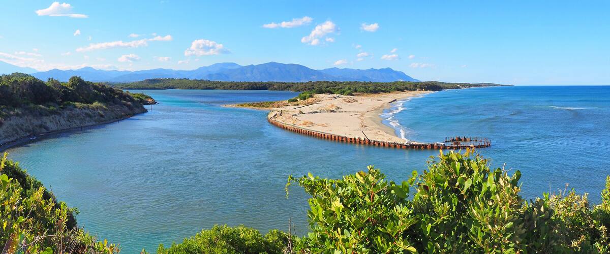 A coastal landscape with a sandy beach, a wooden pier, and mountains in the background.