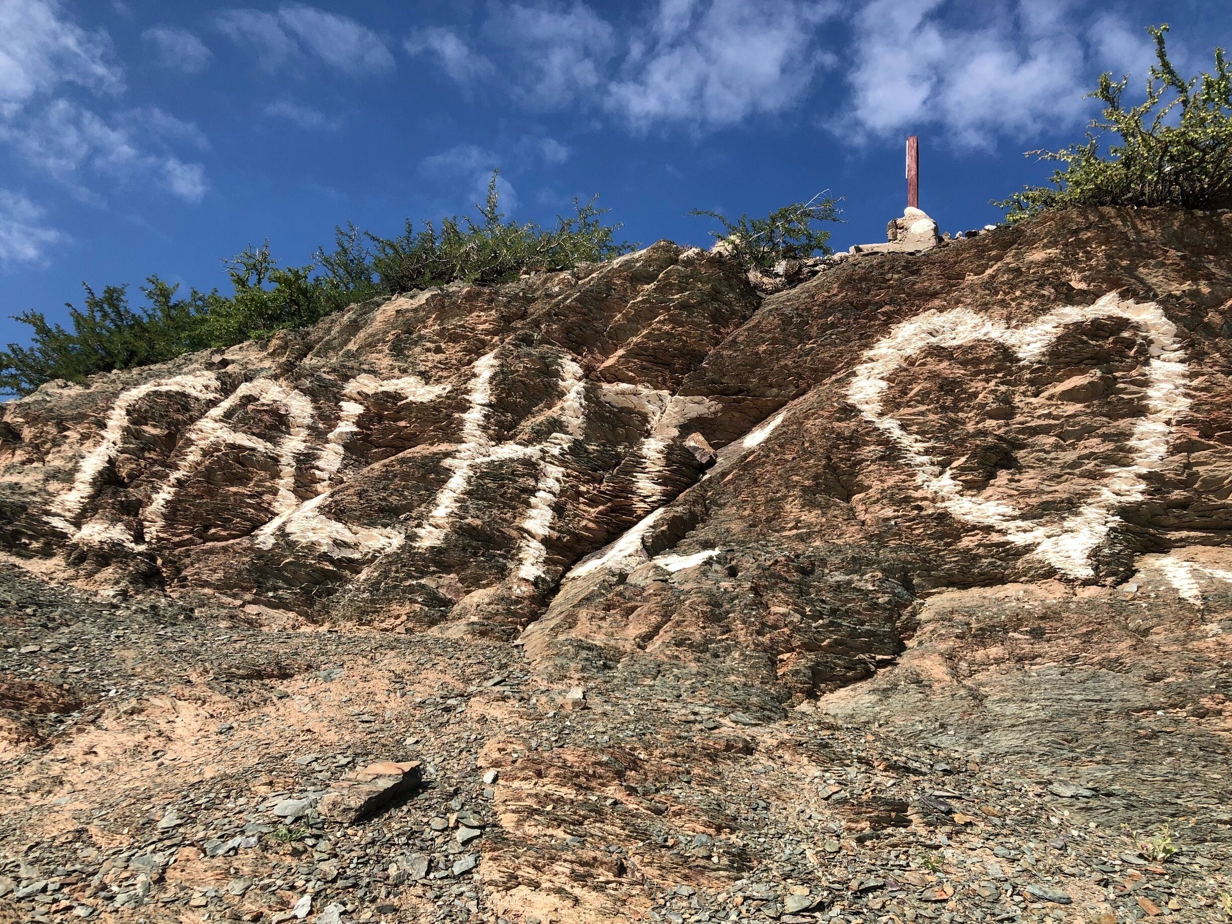 A rocky landscape with a heart-shaped carving and a cross on a hill.