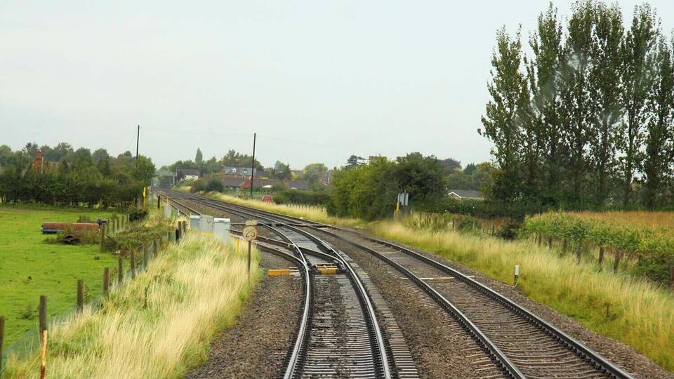 Railway tracks curving through a rural landscape with green fields and trees.