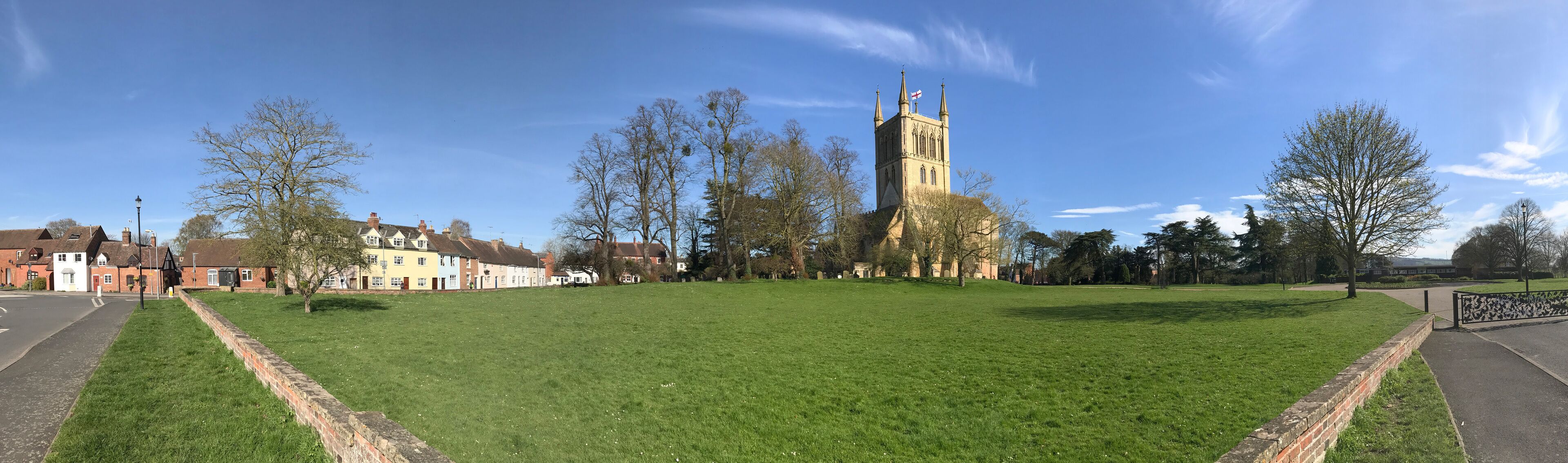 A grassy field with a church tower, residential buildings, and a clear blue sky.