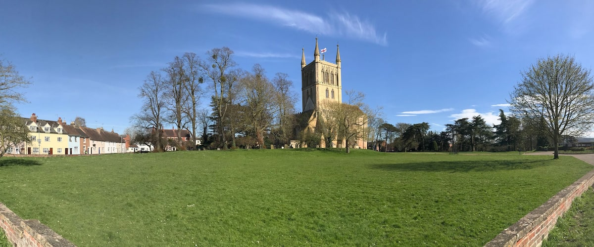 A grassy field with a church tower, residential buildings, and a clear blue sky.