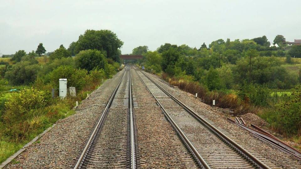 Railway tracks surrounded by greenery and a distant building.