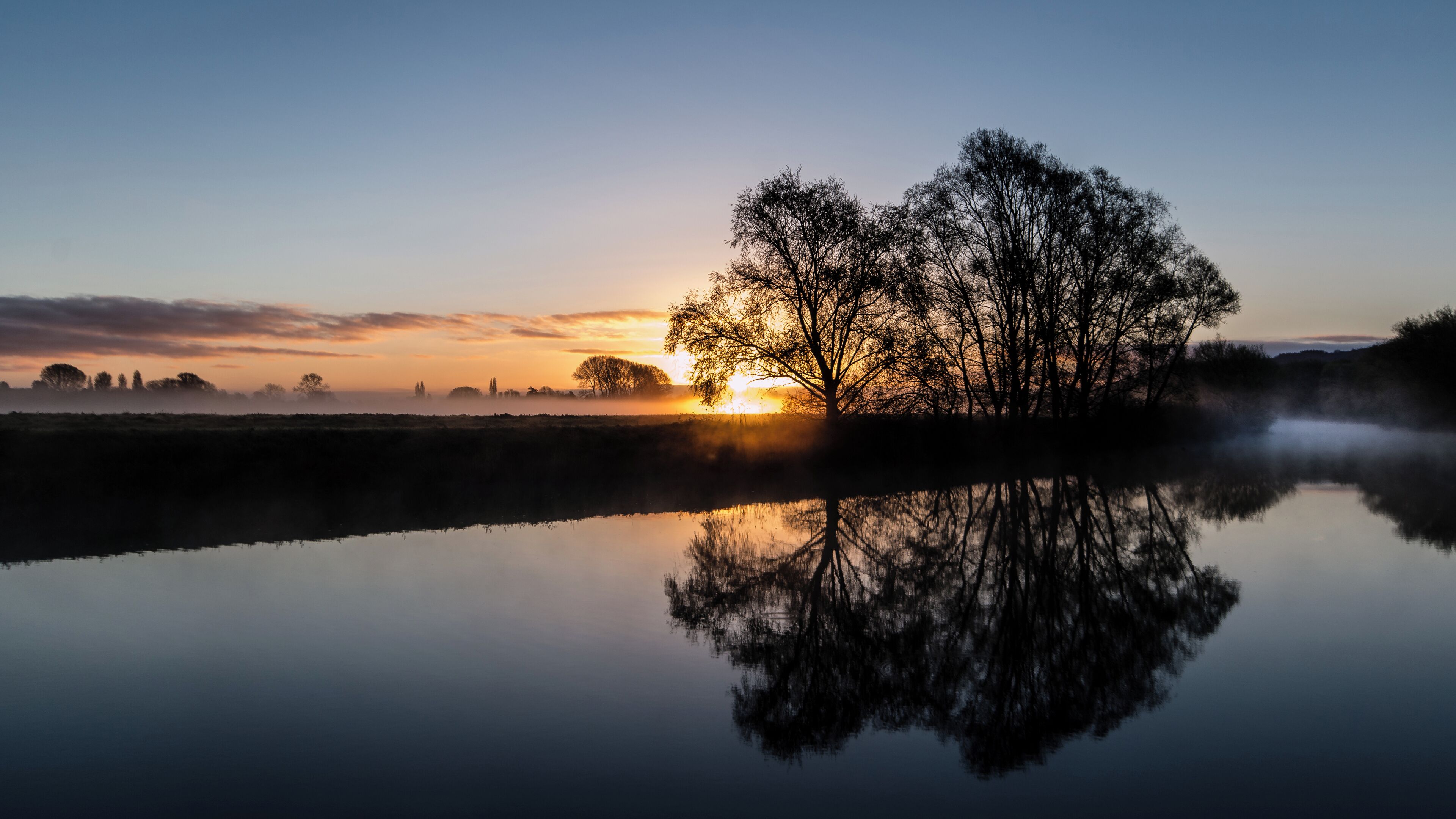 A calm lake reflecting a tree and a sunset.