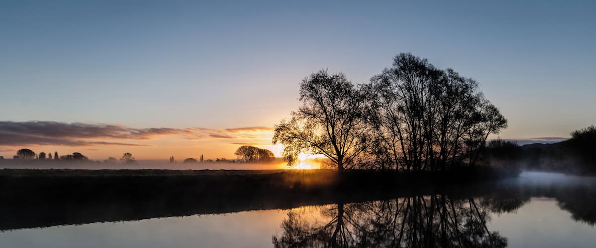 A calm lake reflecting a tree and a sunset.