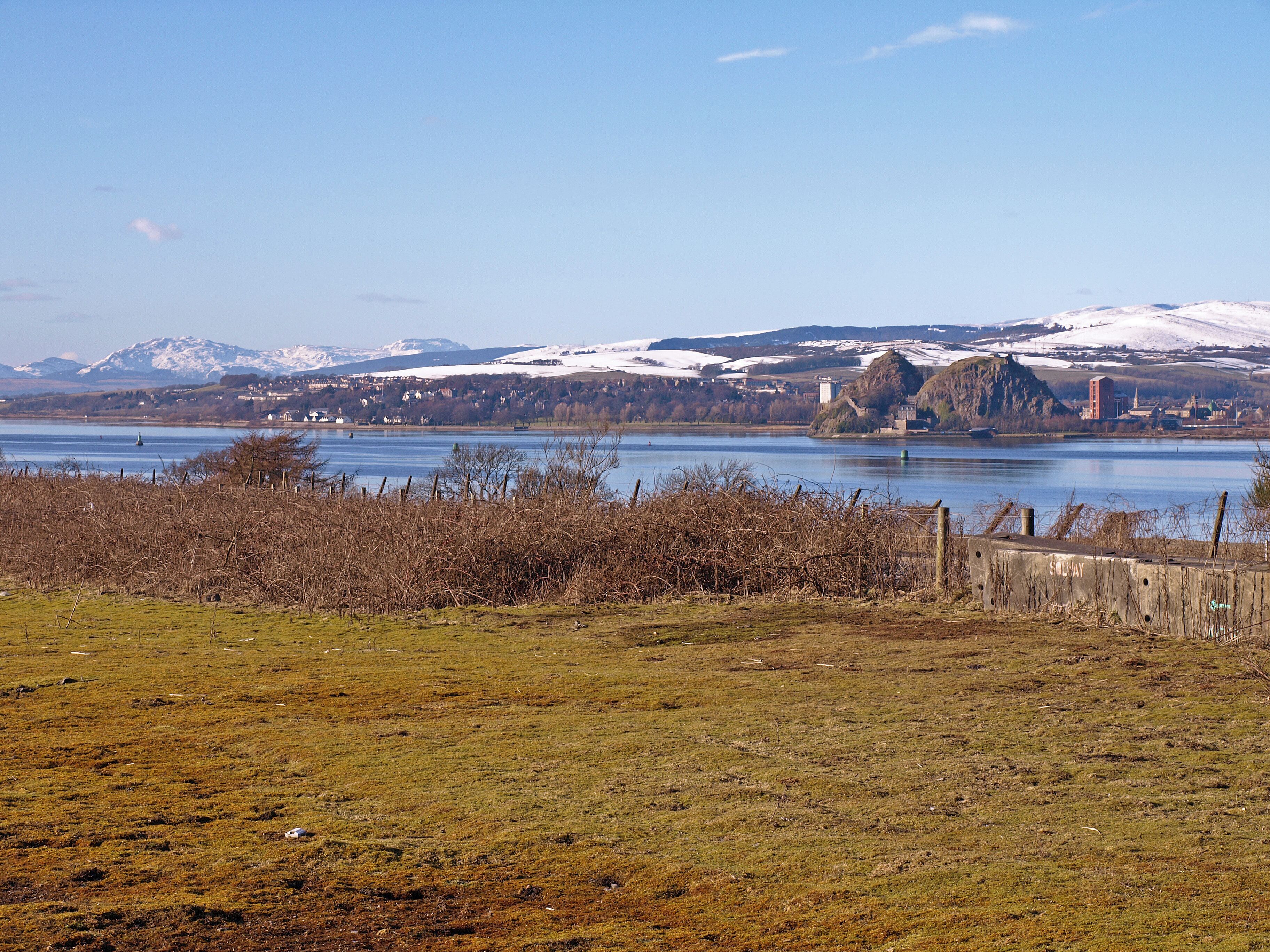 View over the River Clyde Taken from the small road that joins the A8 to the Old Greenock Road. A strange flat piece of land totally covered in moss with blocked off access to A8. Dumbarton Rock across the river. Far in the distance the Cowal Hills.