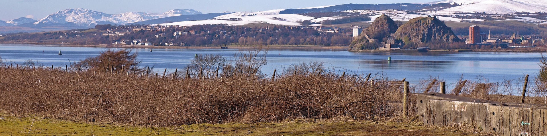 View over the River Clyde Taken from the small road that joins the A8 to the Old Greenock Road. A strange flat piece of land totally covered in moss with blocked off access to A8. Dumbarton Rock across the river. Far in the distance the Cowal Hills.