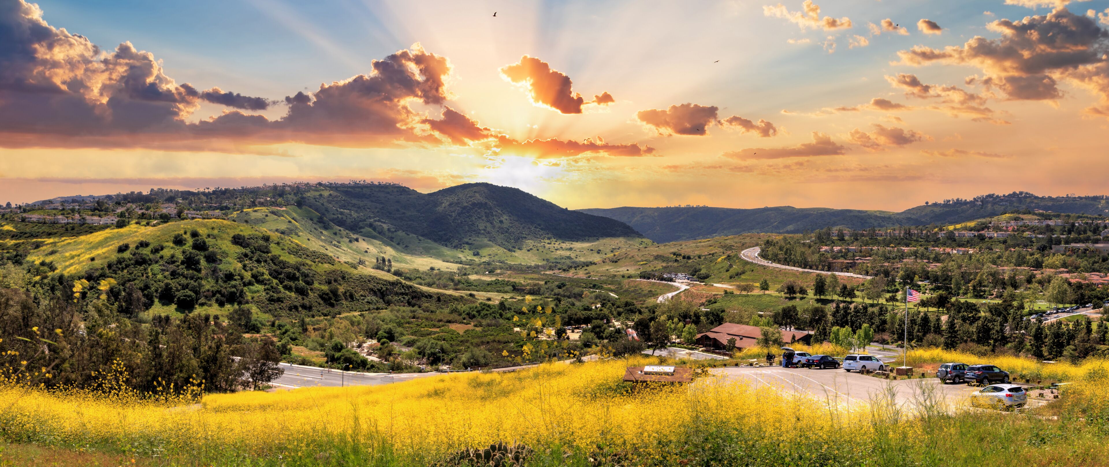 A valley with a winding road, a small settlement, and a mountain in the background.