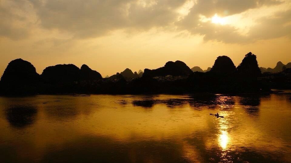 A sunset over a calm body of water with silhouettes of mountains in the background.