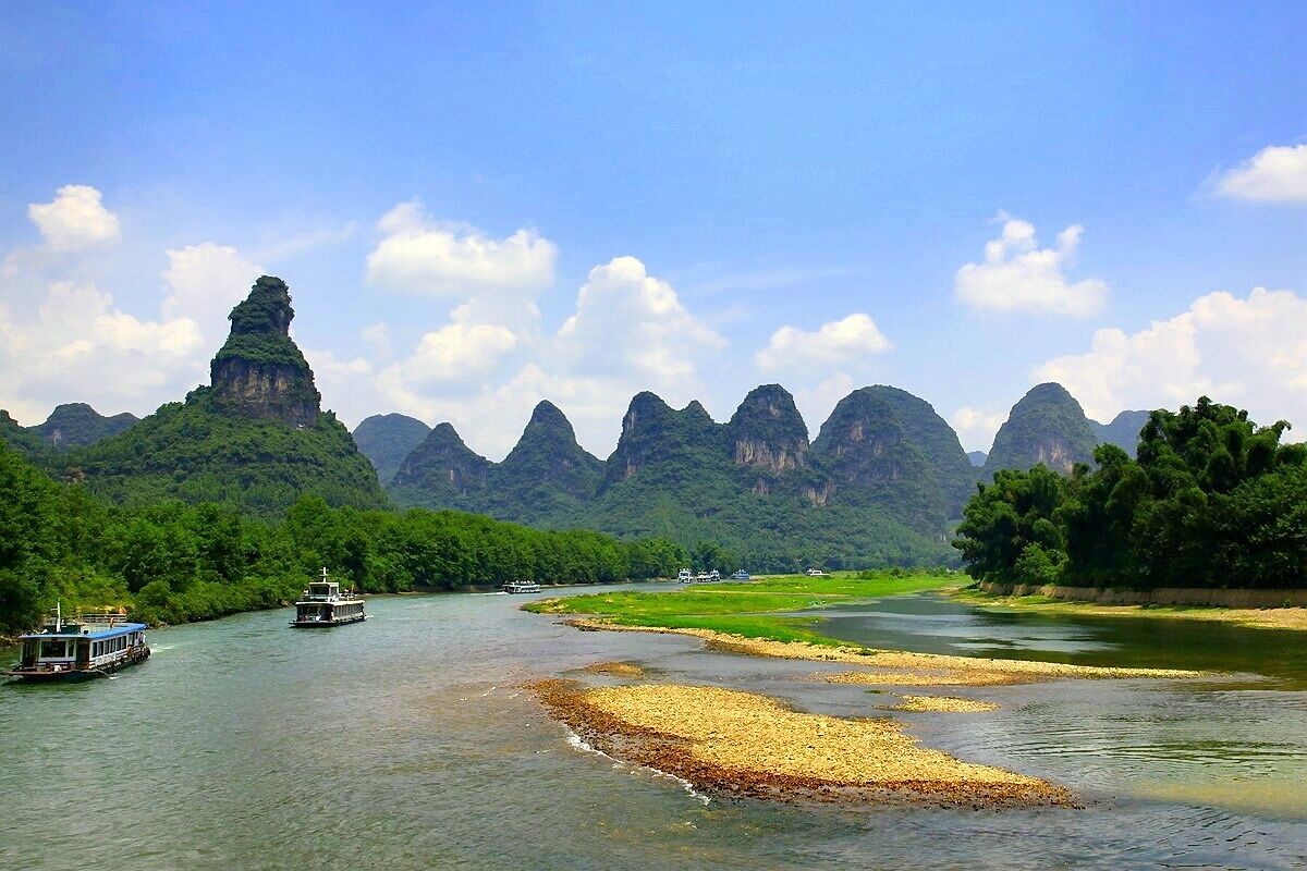 A river with boats, surrounded by lush green hills and a clear sky.