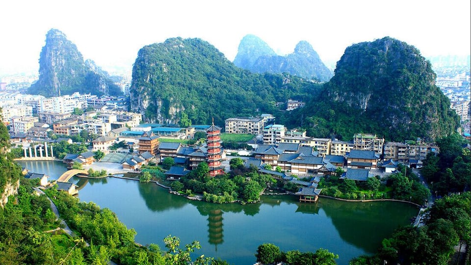 A cityscape with traditional architecture, a prominent pagoda, and surrounding lush mountains.