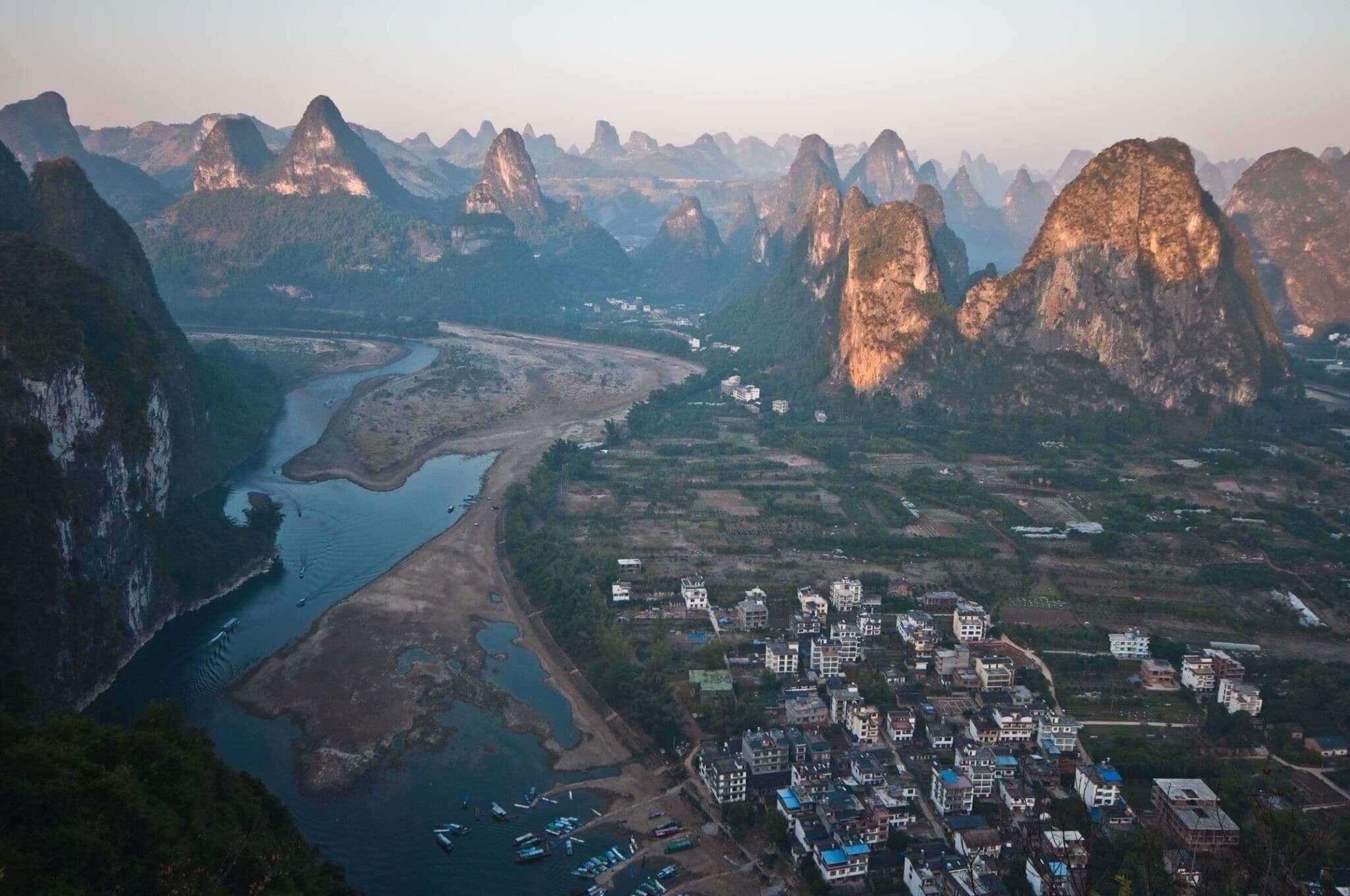 A river winding through a valley with a town and mountains in the background.