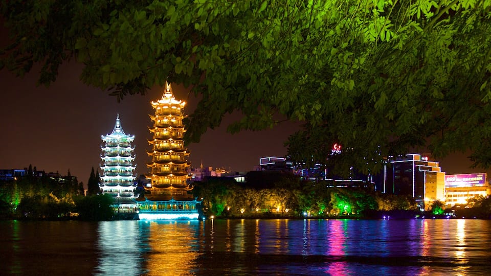 A night view of a traditional pagoda and a modern building by a river.