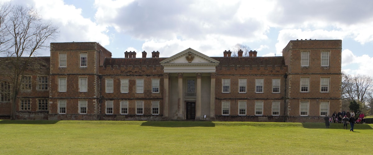 A large, historic brick building with a central entrance and symmetrical wings, surrounded by a well-maintained lawn.