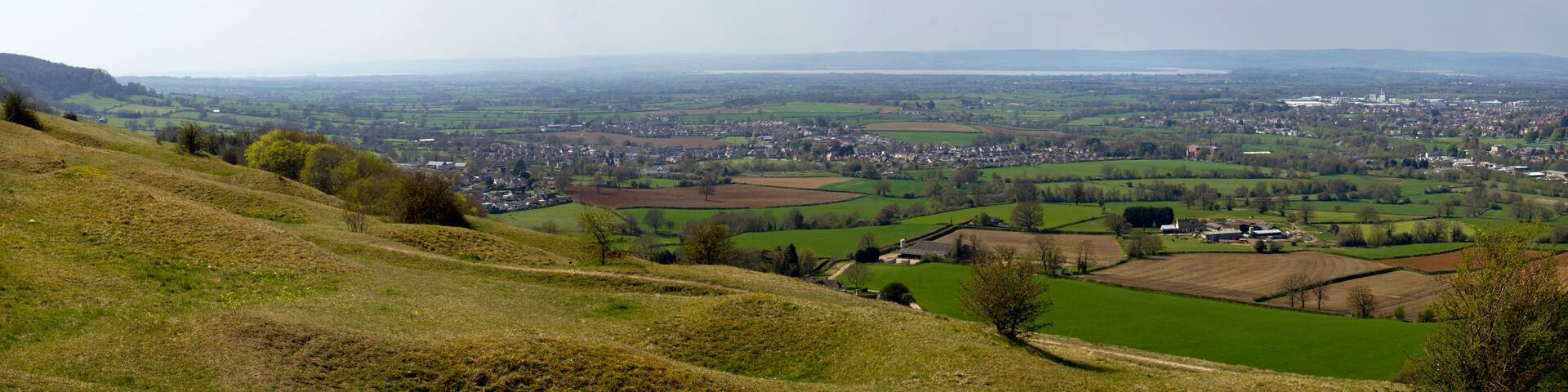 A panoramic view of a rural landscape with rolling hills, fields, and a small town in the valley.