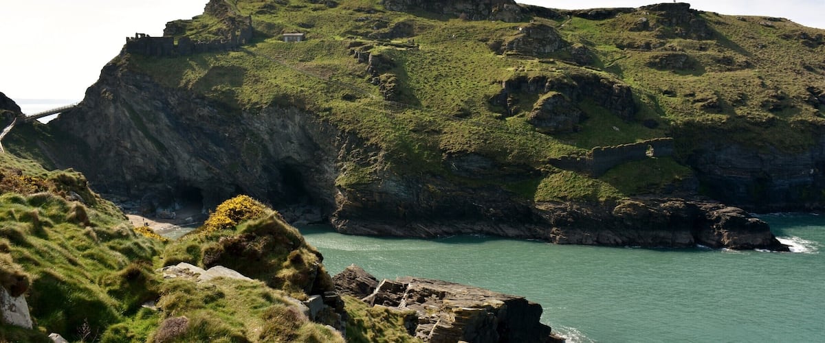 A rugged coastline with rocky cliffs, grassy areas, and a small bridge connecting the land.