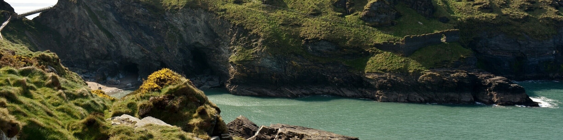A rugged coastline with rocky cliffs, grassy areas, and a small bridge connecting the land.