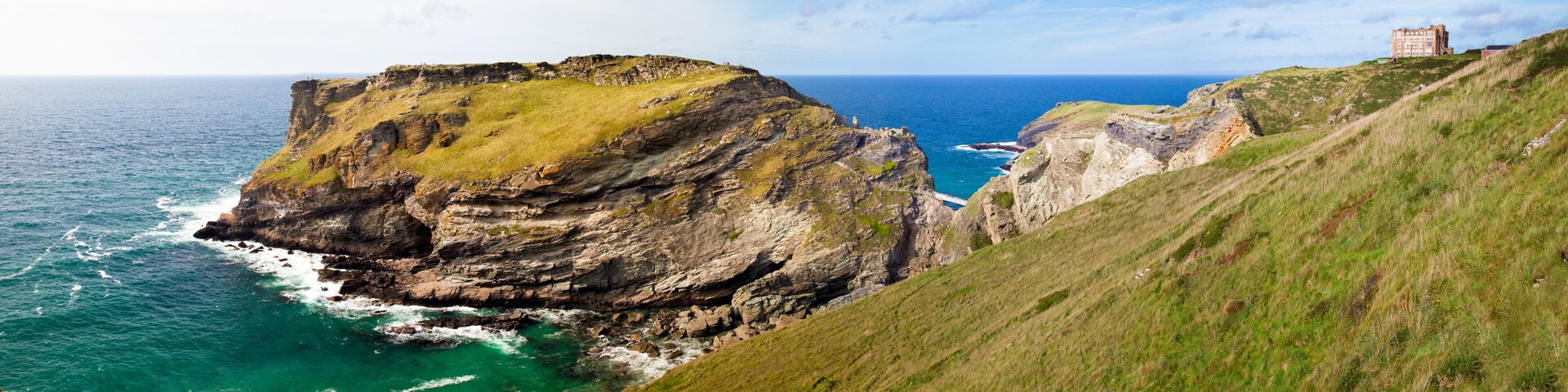 A coastal cliff with a grassy slope and a building in the background.