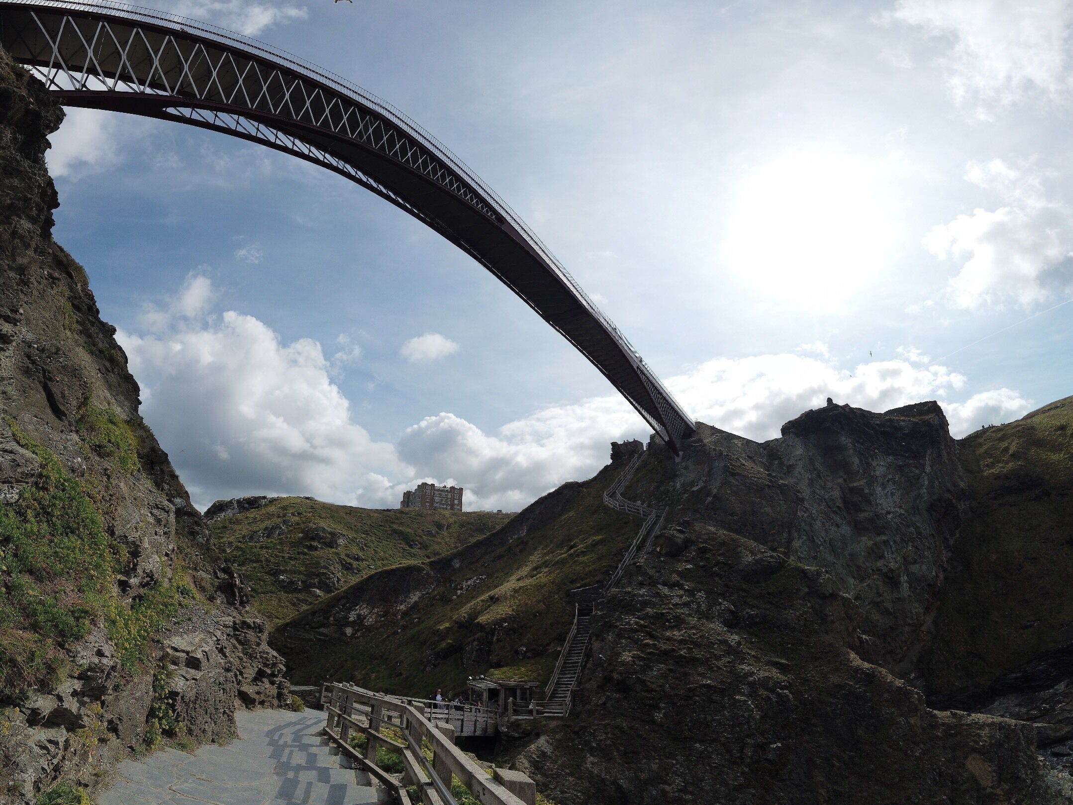 A bridge arching over a valley with a staircase leading up to a building.