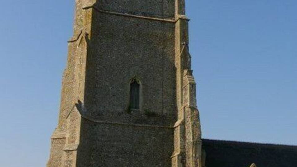 A tall, narrow stone church tower with a small arched window near the top and another arched window below.