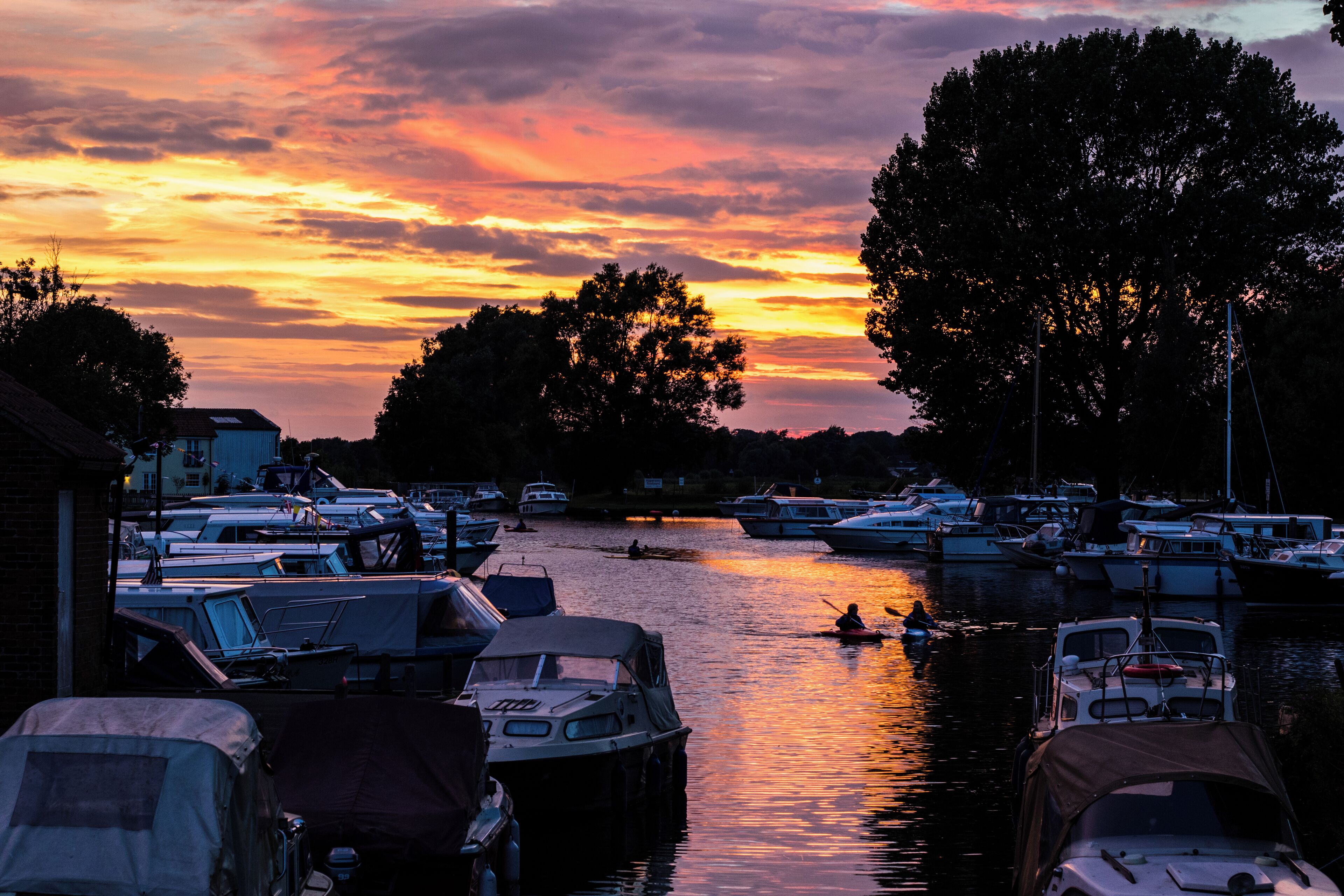 A marina at sunset with boats docked and a person kayaking in the water.