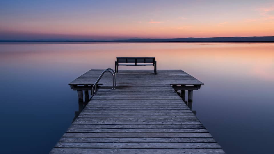 A wooden pier extending into calm water with a bench at the end.