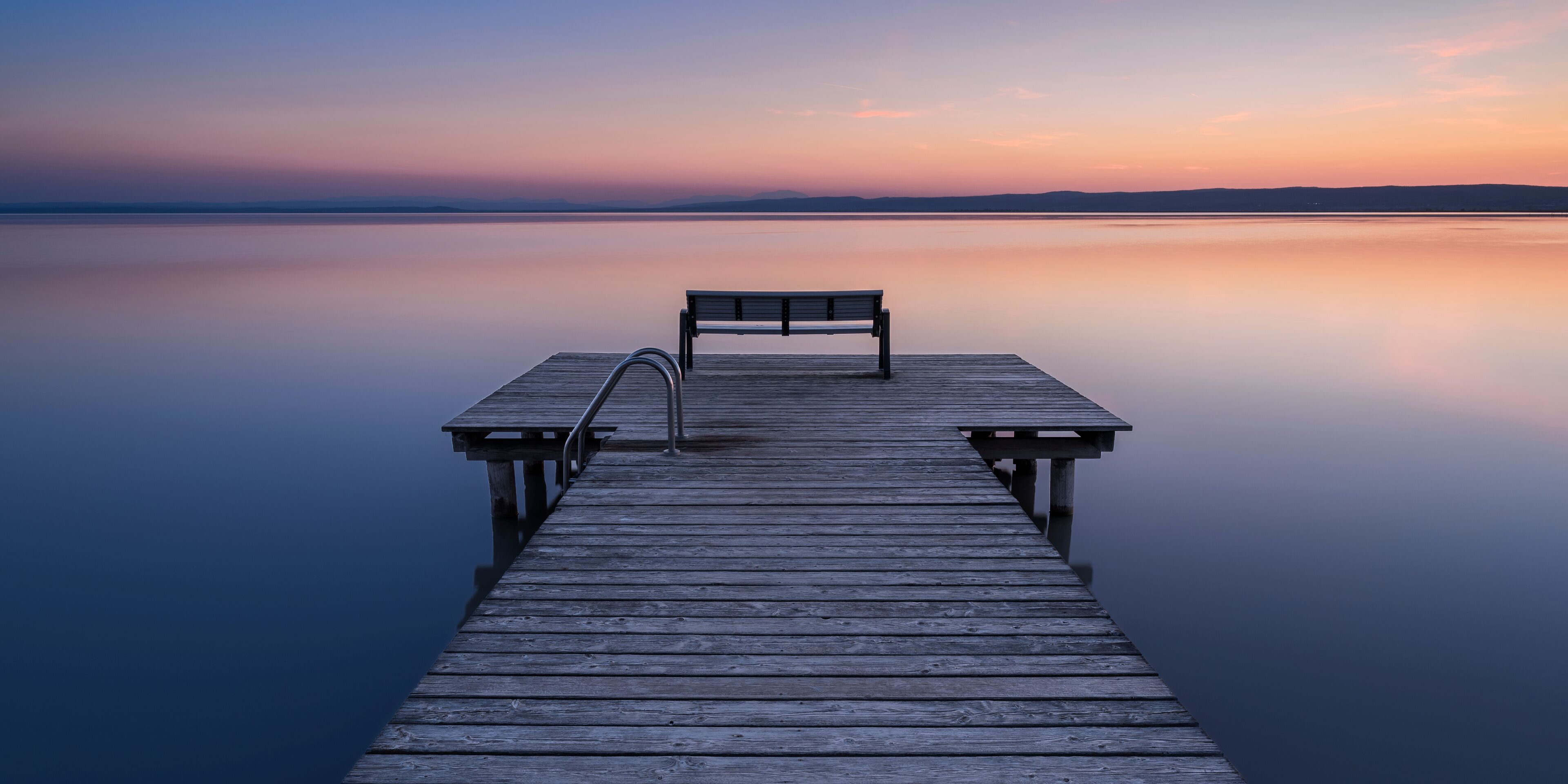A wooden pier extending into calm water with a bench at the end.