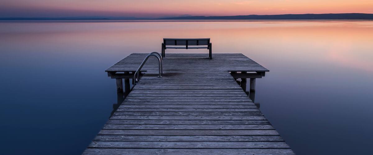 A wooden pier extending into calm water with a bench at the end.