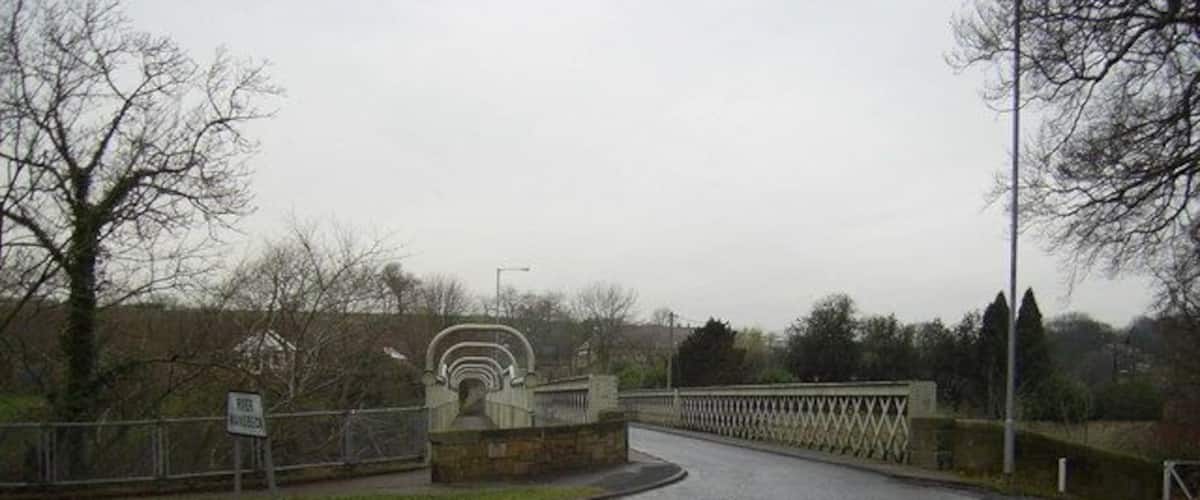 A curved road leading to a stone bridge with a sign indicating a footpath.