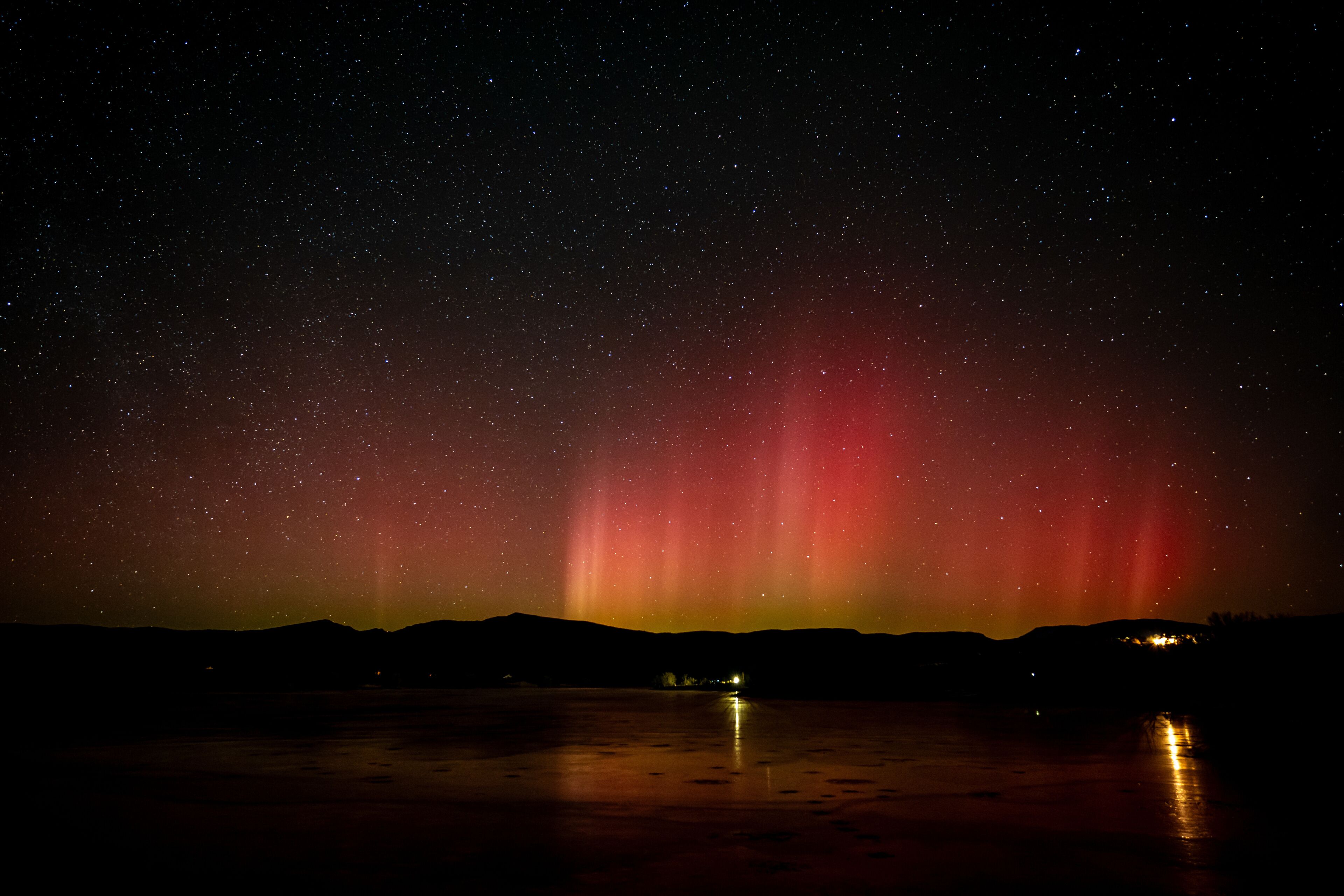 A night sky with stars and a red aurora over a body of water with reflections.