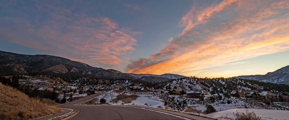 A snow-covered mountain landscape with a winding road and houses at sunset.