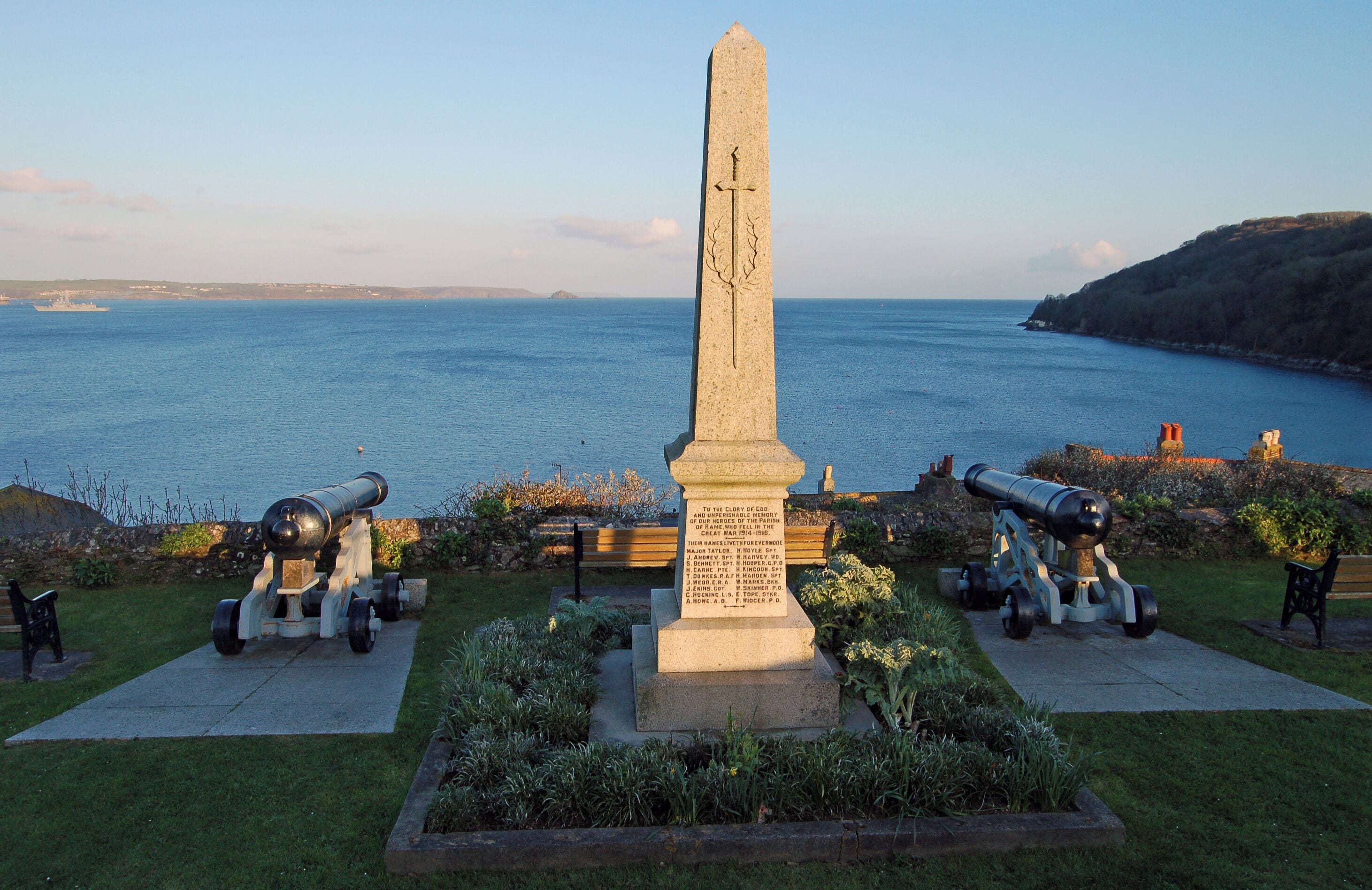 War Memorial in Cawsand, Cornwall. The view is across Plymouth Sound towards Devon. A frigate is entering the sound.