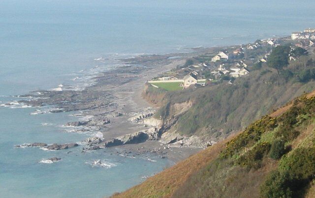 A coastal village with houses on a cliff, rocky shoreline, and the ocean.