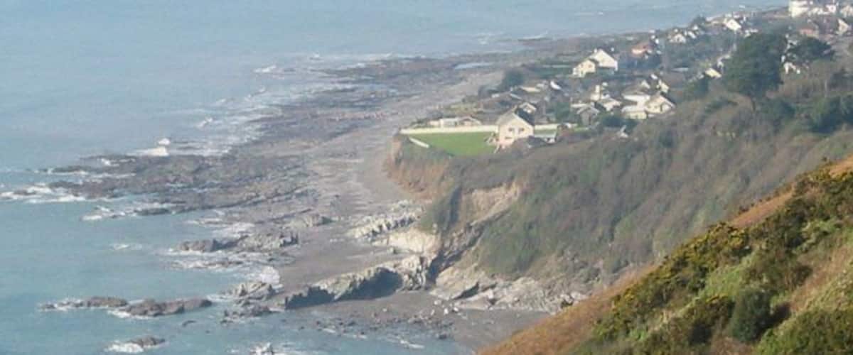 A coastal village with houses on a cliff, rocky shoreline, and the ocean.