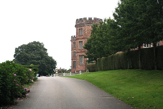 A pathway leading to a castle-like structure surrounded by greenery and a hedge.