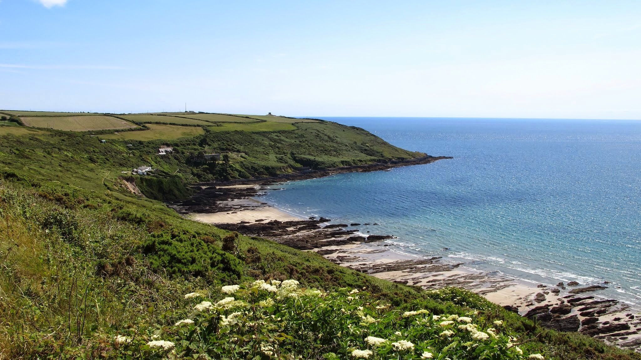 A coastal landscape with a curved shoreline, green hills, and a clear blue sea.