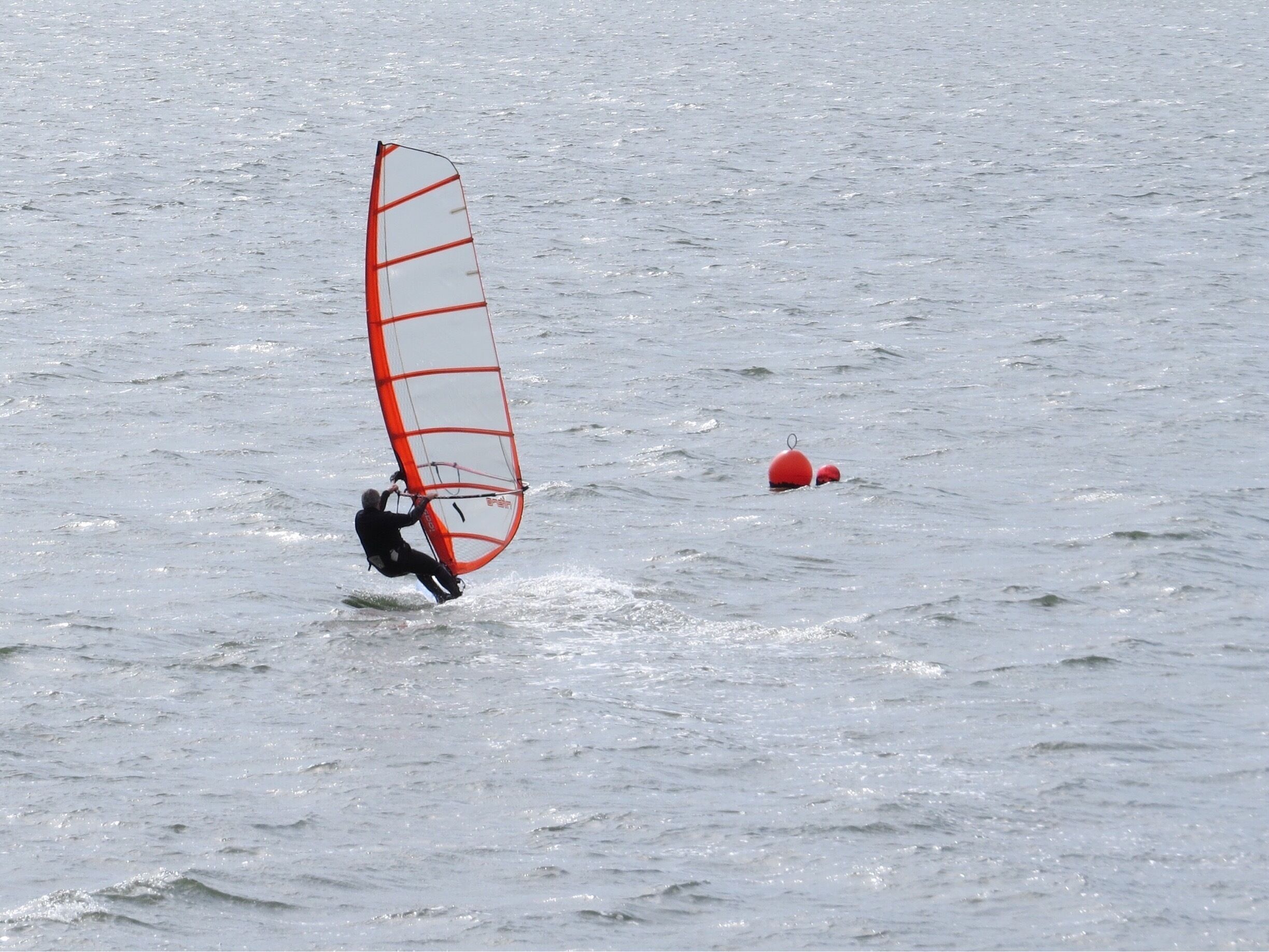 A person windsurfing on a body of water with a red buoy in the background.