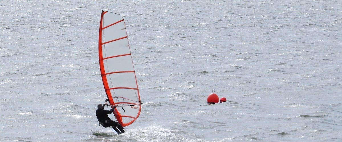 A person windsurfing on a body of water with a red buoy in the background.