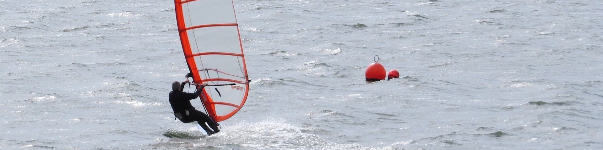 A person windsurfing on a body of water with a red buoy in the background.