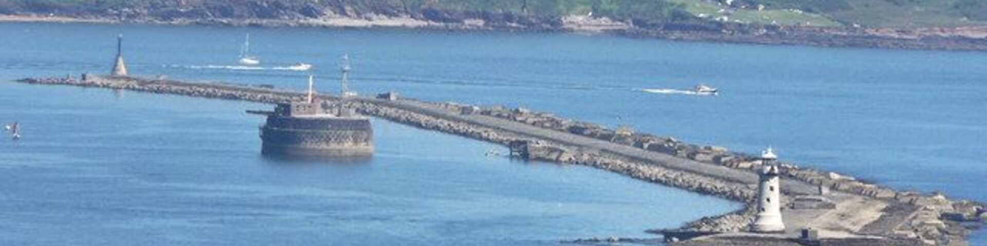 Escena costera con un faro, un rompeolas y una pequeña isla con un edificio.