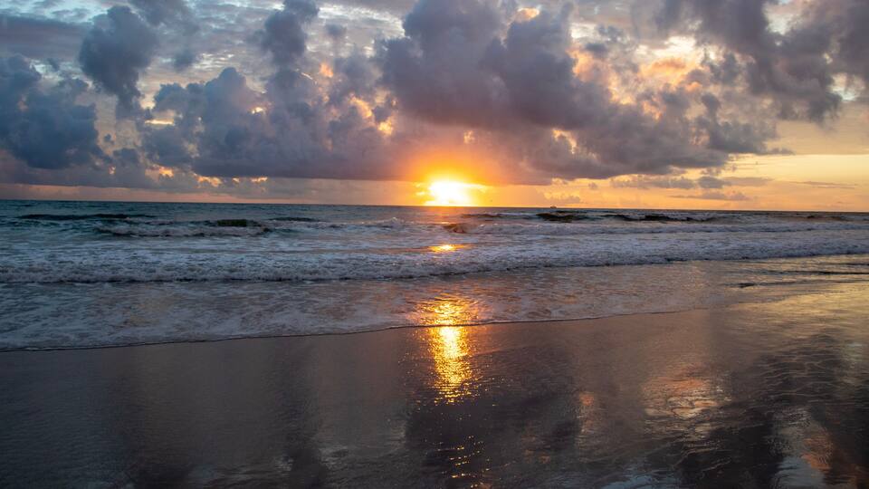 A sunset over the ocean with clouds and waves.