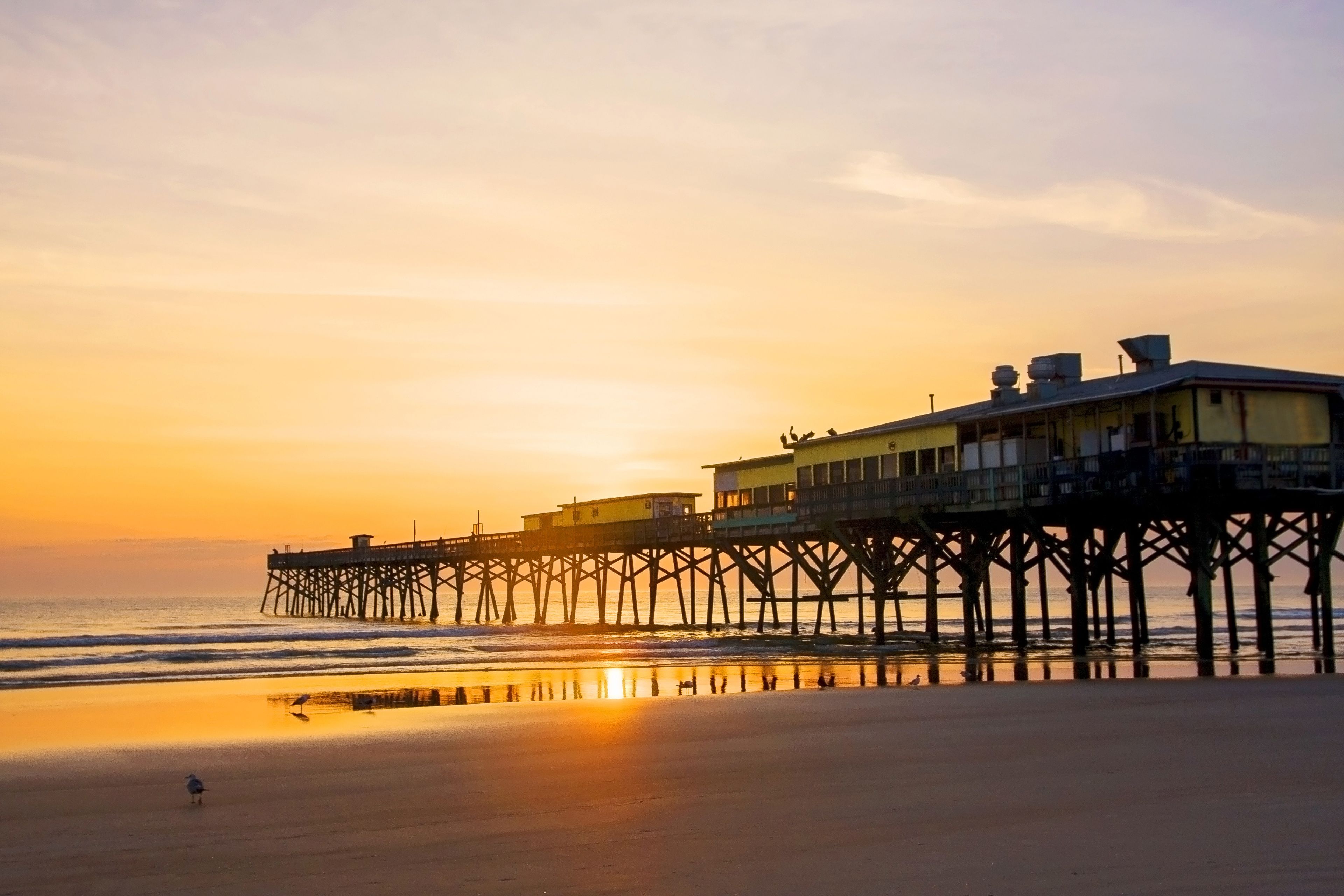 A pier extending into the ocean at sunset with buildings on it.