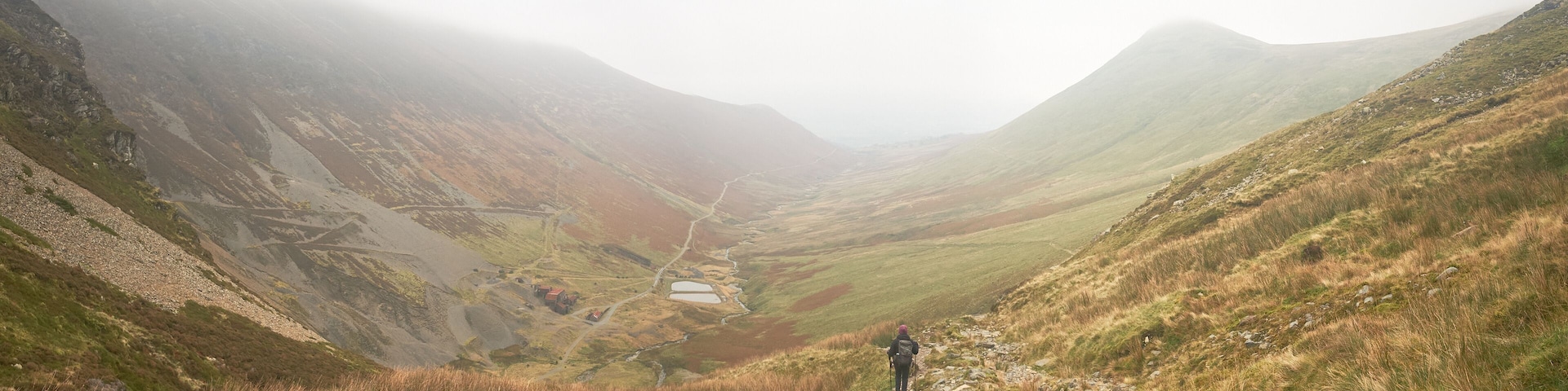 A hiker on a mountain trail with a valley and a small lake.