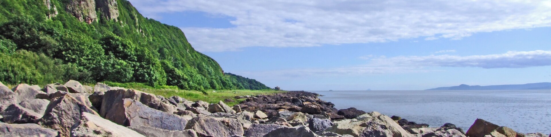 Una costa rocosa con grandes rocas y una ladera verde al fondo.