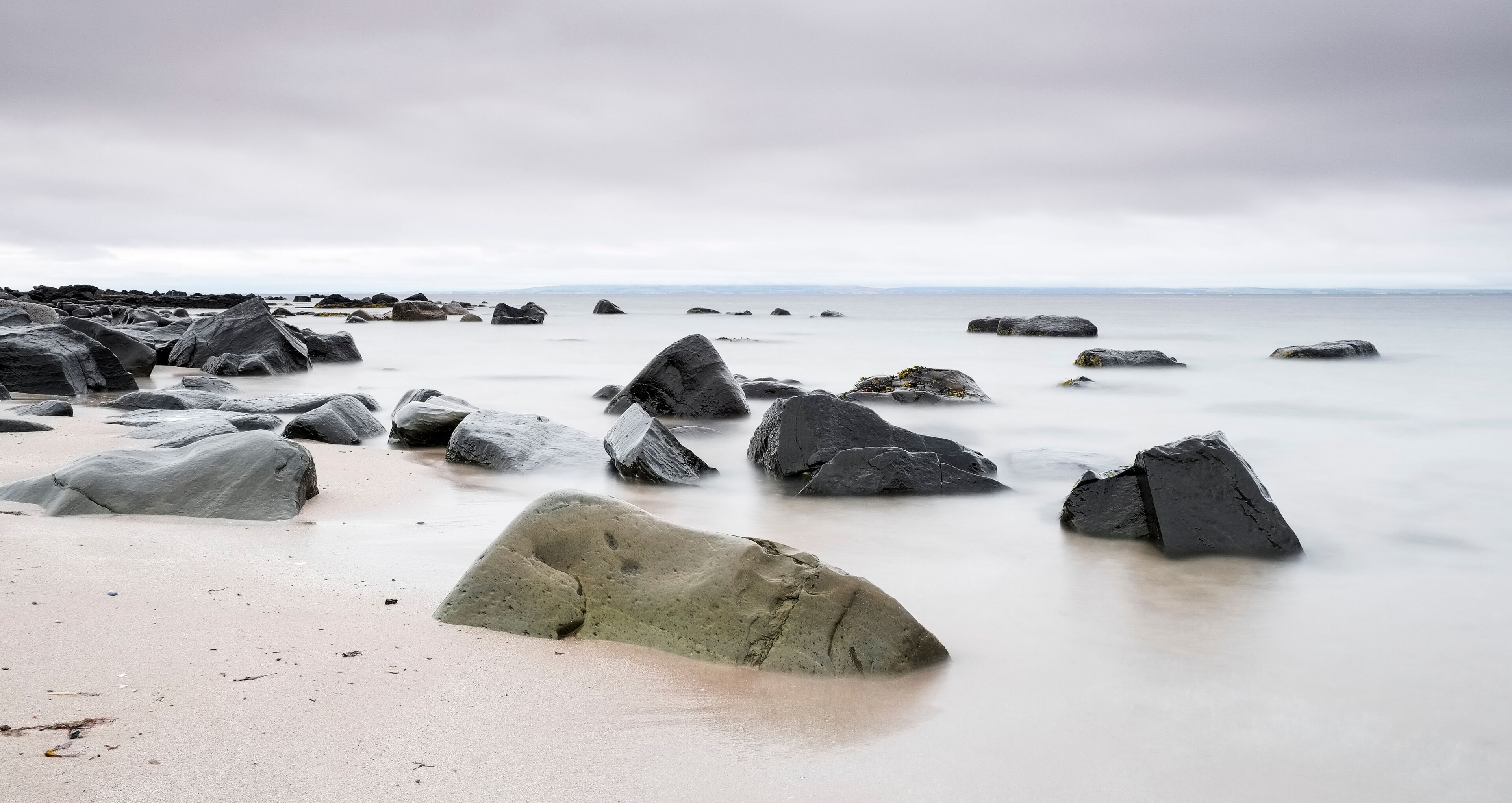 A rocky shoreline with large boulders and a calm sea under a cloudy sky.
