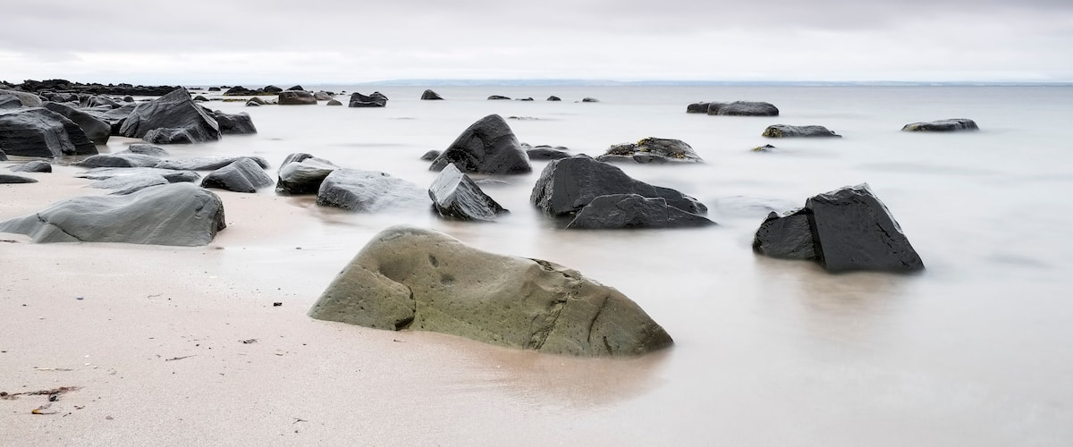 A rocky shoreline with large boulders and a calm sea under a cloudy sky.