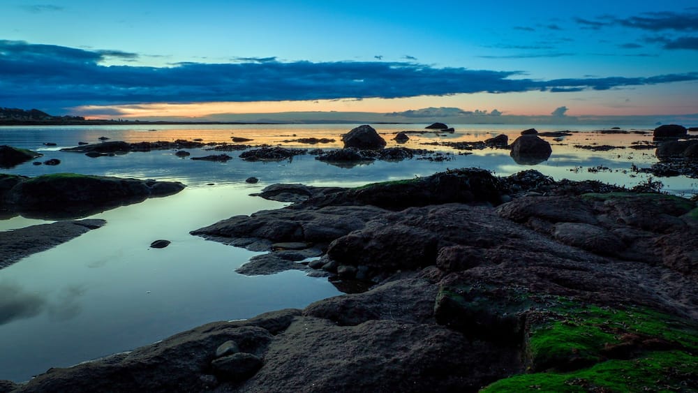 A rocky shoreline with calm water and a sunset in the background.