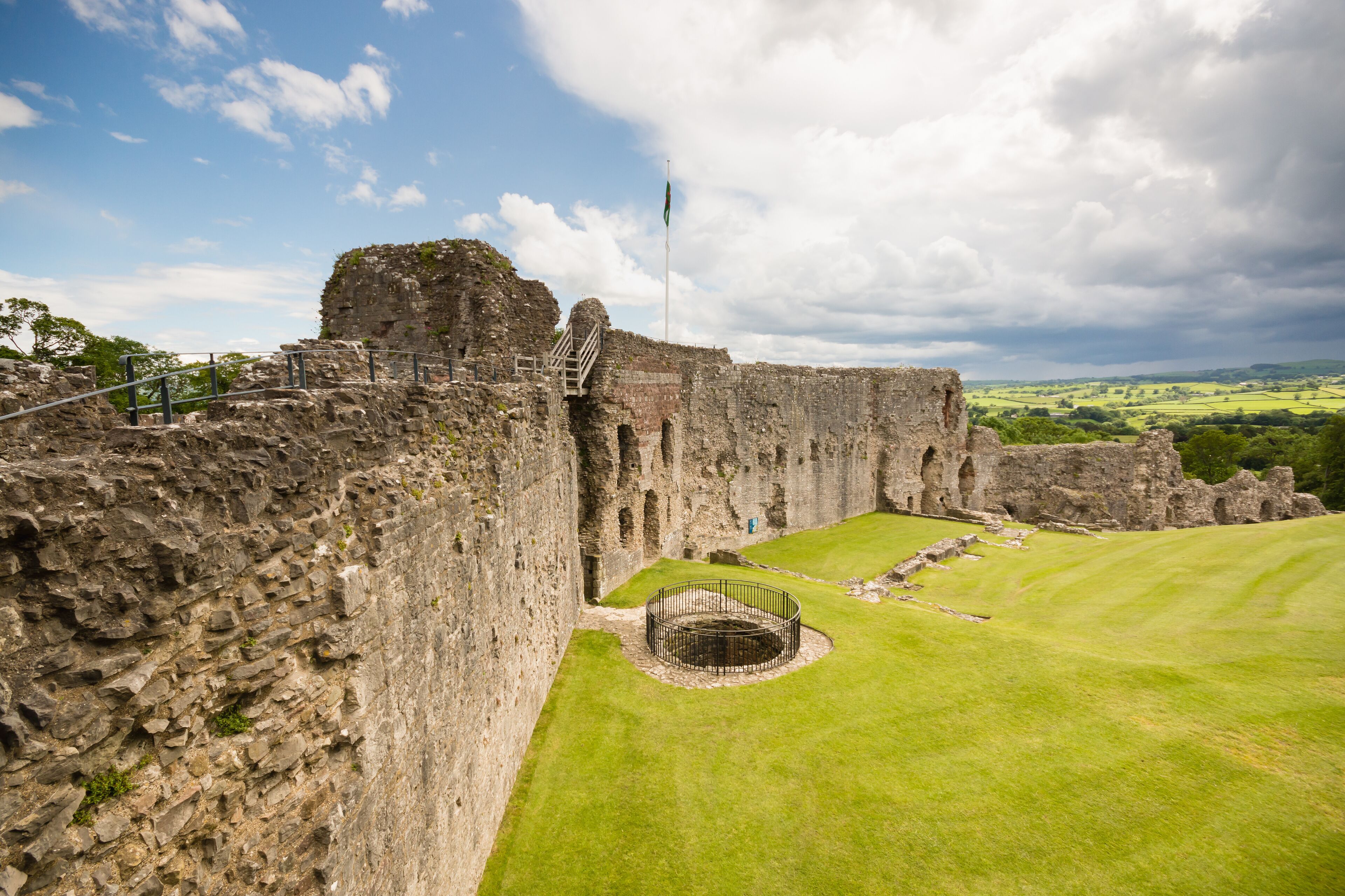 A historic stone castle with a grassy courtyard and a flagpole.