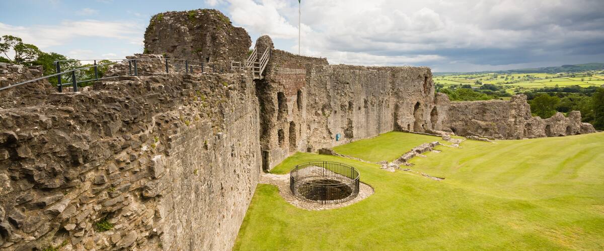 A historic stone castle with a grassy courtyard and a flagpole.
