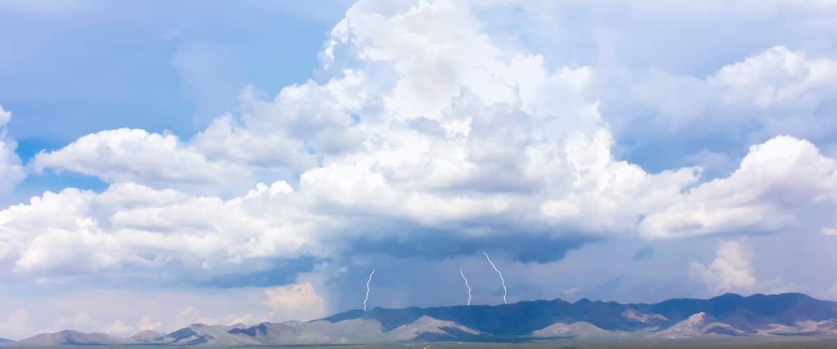 A mountainous landscape with a cloudy sky and lightning strikes.